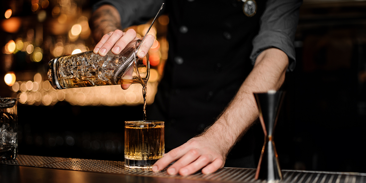 A bartender pouring a cocktail from a shaker